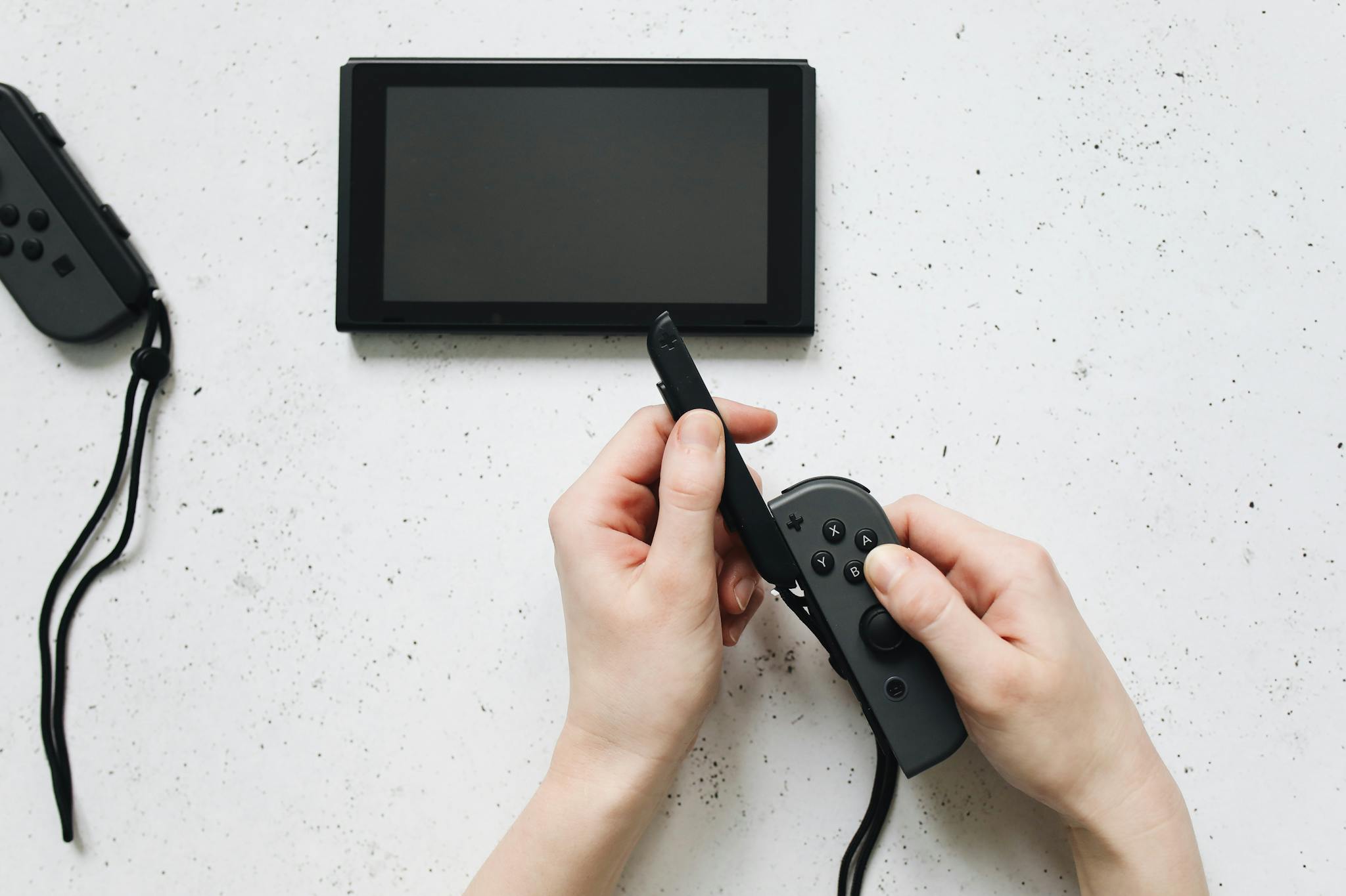 Close-up of hands holding a game controller on a white surface by a portable gaming device.