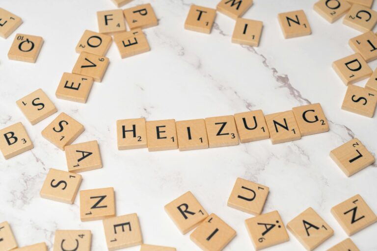 Scrabble tiles spelling 'Heizung' surrounded by scattered tiles on a marble surface.